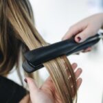 Close-up of a hairstylist using a flat iron on blonde hair in a salon setting.