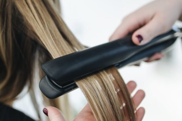 Krijg de Perfecte Look met de Beste Kapper in Den Bosch Close-up of a hairstylist using a flat iron on blonde hair in a salon setting.