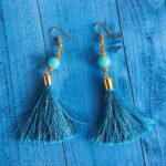 Stylish blue tassel earrings with gold accents displayed on a wooden surface.