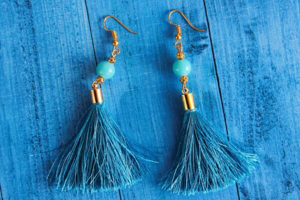 Stylish blue tassel earrings with gold accents displayed on a wooden surface.