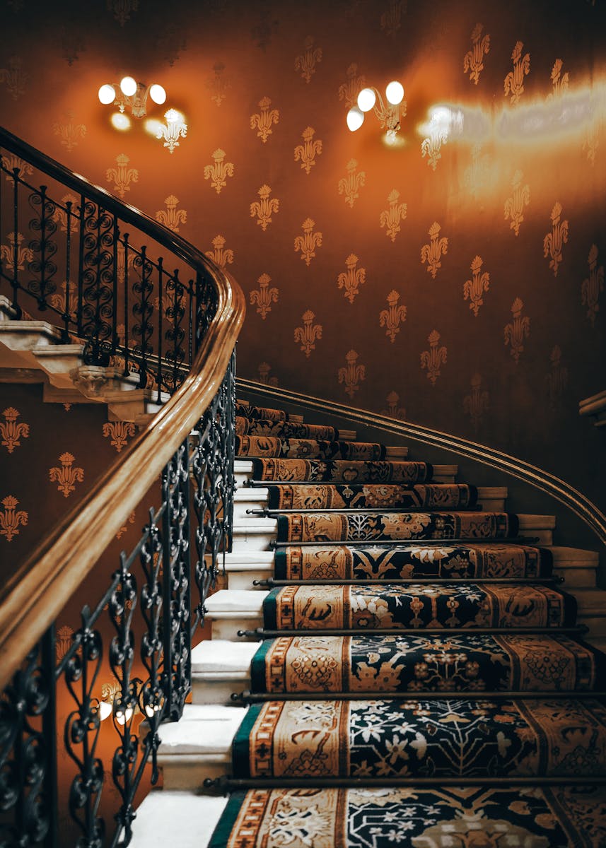 A beautifully detailed vintage staircase with ornate iron handrails and rich patterned carpet.
