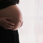 A close-up of a pregnant woman touching her bare belly, expressing warmth and care.