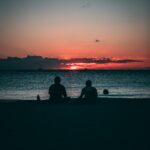 silhouette of two person sitting on sand